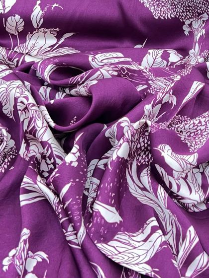 A rich purple modal satin with a bold, tropical-inspired white print. This fabric is perfect for creating a statement piece, be it a dress, gown, or co-ord set.