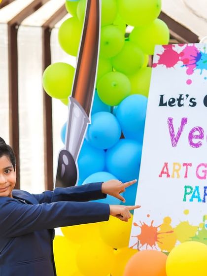 A welcome sign for "Veer's Art Galaxy Party," with the birthday boy pointing excitedly, ready for a day of creative fun.