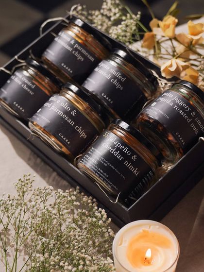 Our Snack Box Hamper, surrounded by delicate flowers and the warm glow of a candle. It’s a thoughtful gift designed for those long chats and happy moments with your siblings.