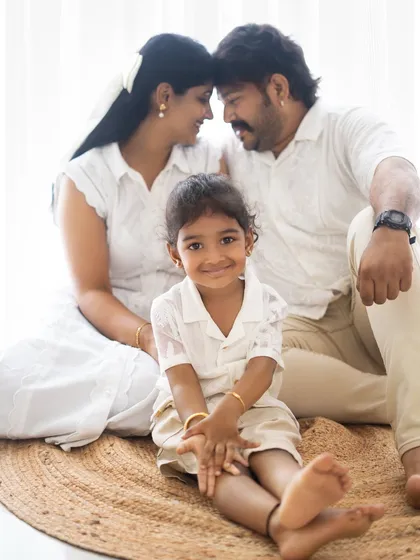 A sweet family portrait with the daughter in the foreground. The parents look at each other lovingly in the background, creating a layered and emotional image.