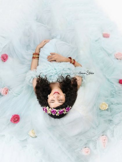 An alternate angle of the dreamy overhead shot, capturing a sweet smile from the mother-to-be as she lies in a cloud of blue tulle and roses.