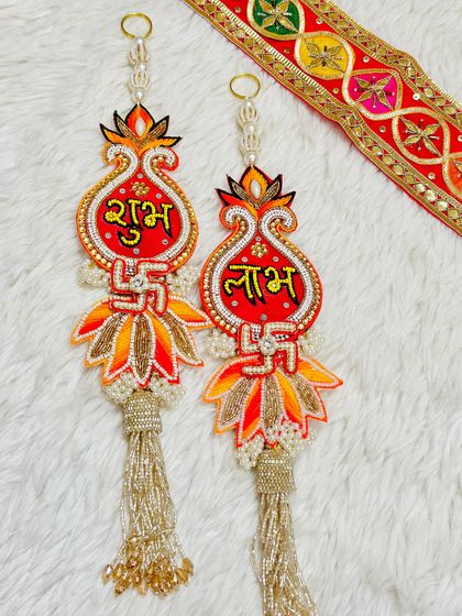 This diya-shaped Shubh Labh hanging is perfect for the festival of lights. The design features a swastika and intricate orange and red beadwork.