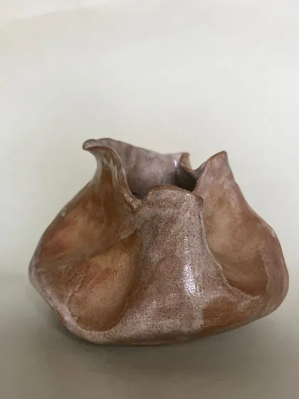 A close-up of a hand-pinched pot with a soft, warm glaze. The organic shape feels so comforting to hold.