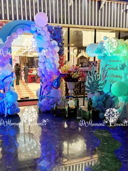A stunning mermaid-themed entrance under dramatic blue lighting, with balloon arches that mimic waves and underwater bubbles.