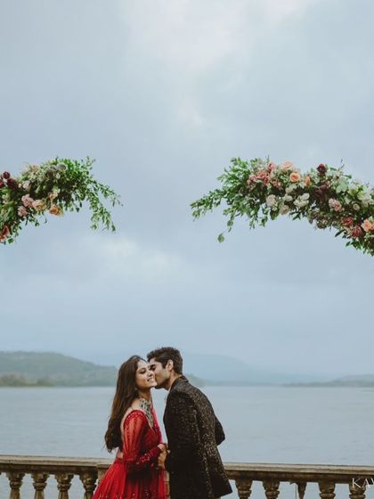 A romantic kiss under a heart-shaped floral arch, set against a serene lake. This is a perfect example of a planned, yet emotionally resonant pre-wedding photograph.