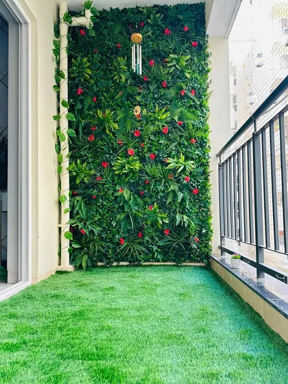 A closer look at a floral balcony installation. The red flowers are evenly distributed among the green leaves, and a hanging wind chime adds a personal touch to the serene space.