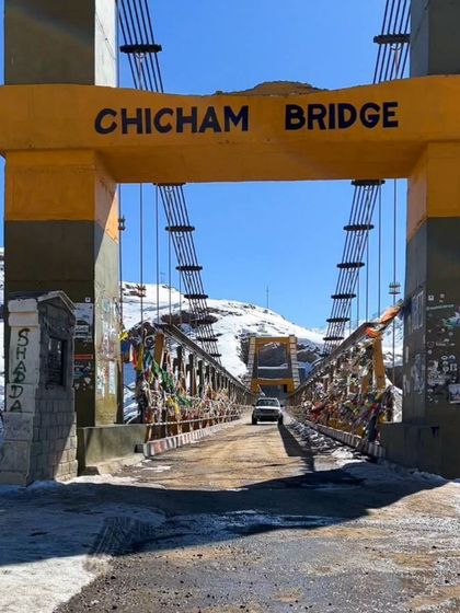 A ground-level view of the Chicham Bridge, showing a car crossing it. This perspective complements the aerial shots, giving a sense of the on-the-ground experience.
