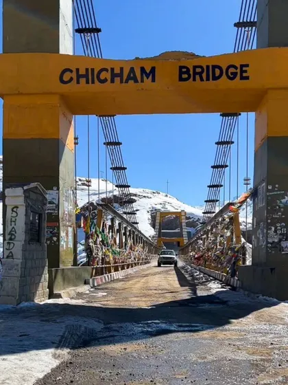 A ground-level view of the Chicham Bridge, showing a car crossing it. This perspective complements the aerial shots, giving a sense of the on-the-ground experience.