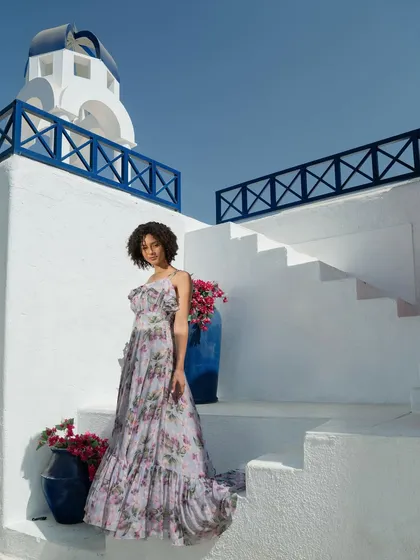 A campaign image for Tangerine Tiger, shot on a Santorini-inspired set. The white and blue architecture provides a beautiful, clean backdrop for the floral maxi dress, creating a destination-wear vibe.