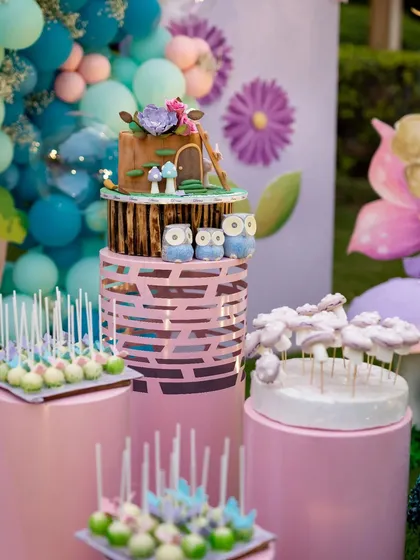 The dessert table is a centerpiece of the celebration. This three-tiered woodland cake, surrounded by themed cake pops and treats, is perfectly integrated into the fairyland decor with its own set of magical mushrooms.