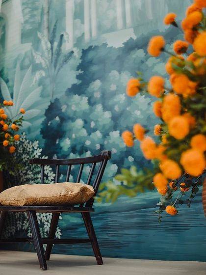 A simple chair set against the hand-painted backdrop of the Varapuja mandap, surrounded by pots of marigolds.