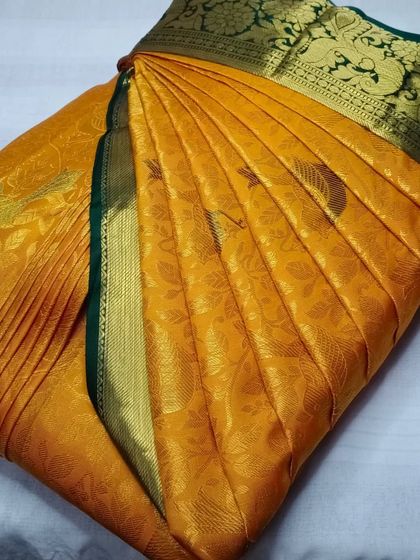 A bright yellow saree with a dark green border. The pleats are neatly arranged to showcase the texture and color of the fabric.