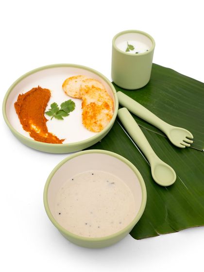 A top-down shot of a kids' dining set styled with idli and chutney on a banana leaf. This creative styling is culturally relevant and visually appealing.
