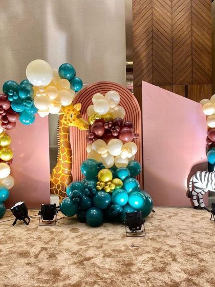 This abstract jungle theme uses geometric pink backdrops with giraffe and zebra cutouts, complemented by artistic balloon arrangements in rich jewel tones.