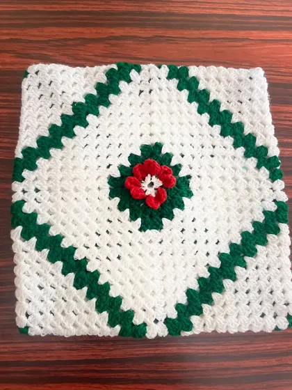 This is the front of a custom granny square cushion cover, featuring a simple yet elegant design with a central floral motif in red, green, and white.