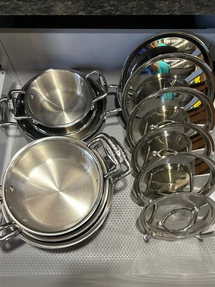 A drawer filled with steel serving bowls and lids, organized using racks to keep them stable and easy to access.