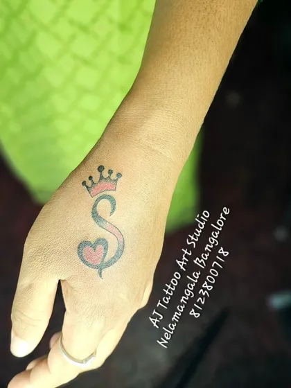 An initial 'S' with a crown and a heart, inked on the back of the hand.