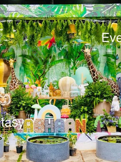 An incredibly detailed and lush jungle setup for Eshaan's birthday. The scene is filled with hanging foliage, a variety of animal figures like tigers and flamingos, and small water pools to create a truly immersive tropical jungle experience.