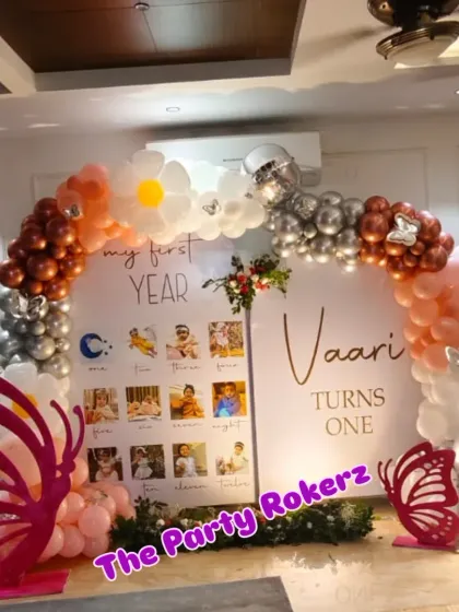 A unique take on the butterfly theme for a first birthday. This setup includes a "My First Year" photo display board, a balloon arch with daisy accents, and large pink butterfly cutouts.