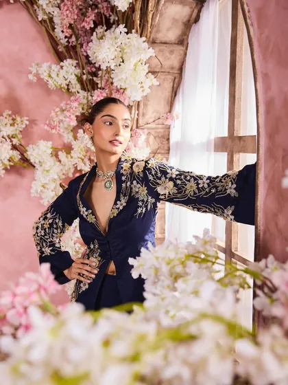An elegant pose by the window, framed by flowers. The makeup is kept classic and timeless to complement the intricately embroidered navy blue jacket.