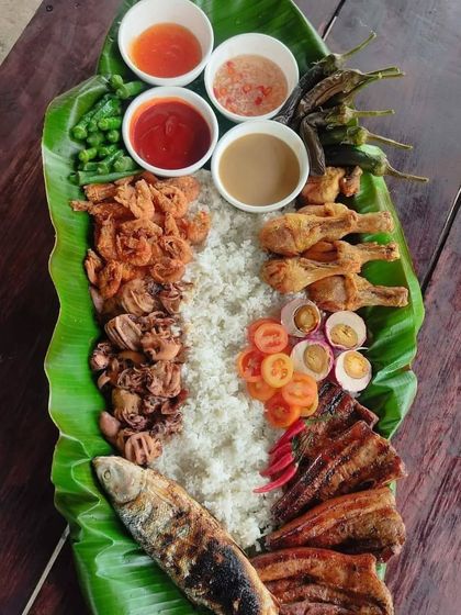 For a unique and communal dining experience, we can arrange a traditional Kamayan feast. A generous spread of rice, grilled fish, fried calamari, chicken, and fresh salads is laid out on banana leaves for everyone to share.