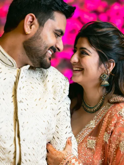A candid shot of the happy couple sharing a laugh, with a vibrant pink floral background adding to the celebratory mood.