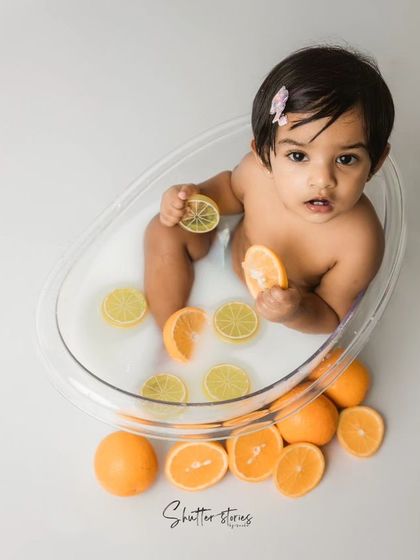 A refreshing fruit bath! This little girl enjoys a milk bath with slices of orange and lemon, a fun and colorful splash session.