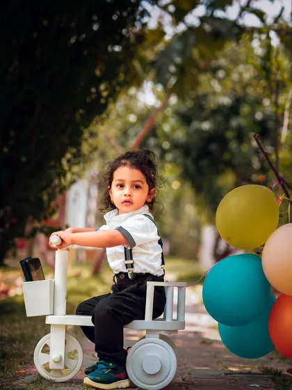 Ready for a ride. The path and colorful balloons create a sense of journey and fun in this outdoor toddler portrait.