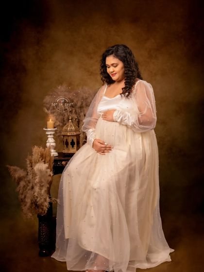 A quiet moment of reflection for this mom-to-be, seated gracefully amidst a candlelit, vintage-inspired studio setup.