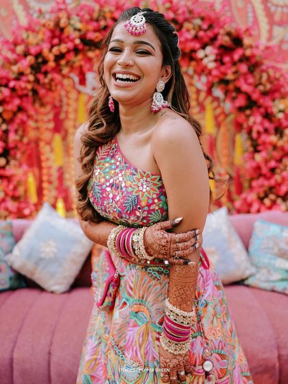 A joyful, laughing portrait of the bride, Arya, during her Mehendi or Sangeet ceremony. Her colorful outfit and carefree expression are infectious.