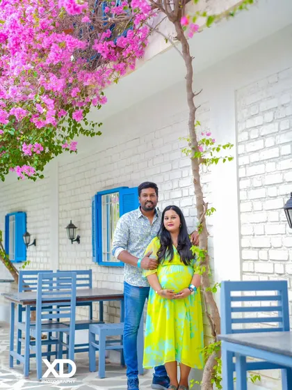 A full-length portrait of a couple in a charming outdoor cafe setting with blooming flowers.