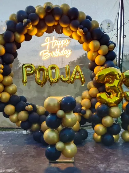 I design sophisticated decorations for milestone birthdays, like this stylish setup for a 35th celebration. It features a full ring backdrop covered in classic black and metallic gold balloons. To make it personal, I add large gold foil balloons for the name and age, along with a bright neon sign.