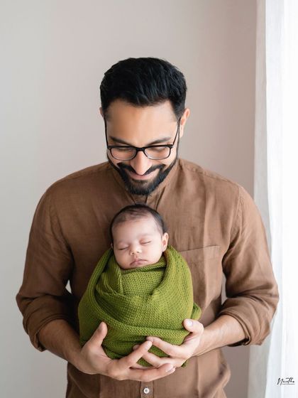 A proud father holding his sleeping newborn, wrapped in a cozy green swaddle.