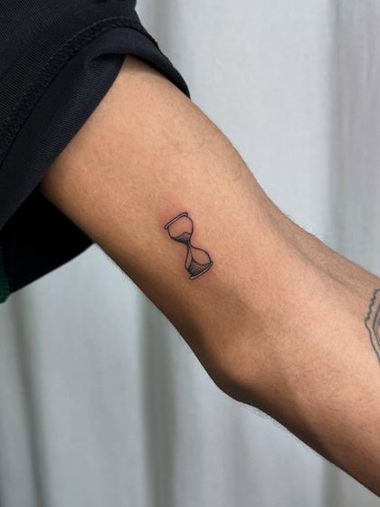 A minimalist hourglass tattoo, symbolizing the finite nature of time. This was created as part of a memorial set, representing precious moments shared with a loved one.
