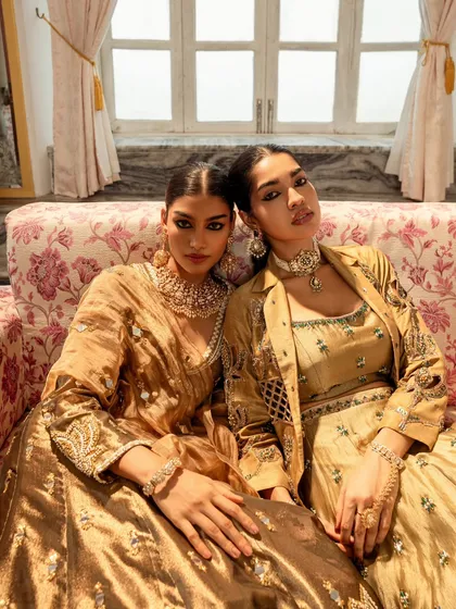 Two models seated together, creating a powerful image of shared elegance for a brand campaign. The lighting is designed to bring out the metallic sheen and embroidery of the coordinated outfits.