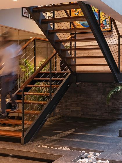 This staircase design seamlessly integrates with the living space, featuring an open-riser construction that allows light to flow through. The mix of steel, wood, and a stone accent wall creates a dynamic and modern transition.