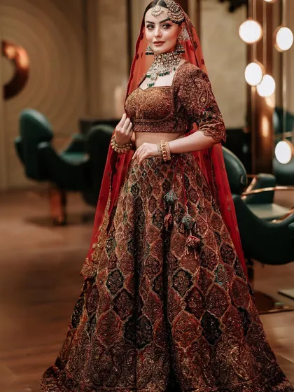A full view of a bride in a stunning rust-colored lehenga. The jewellery adds a touch of antique charm and elegance.