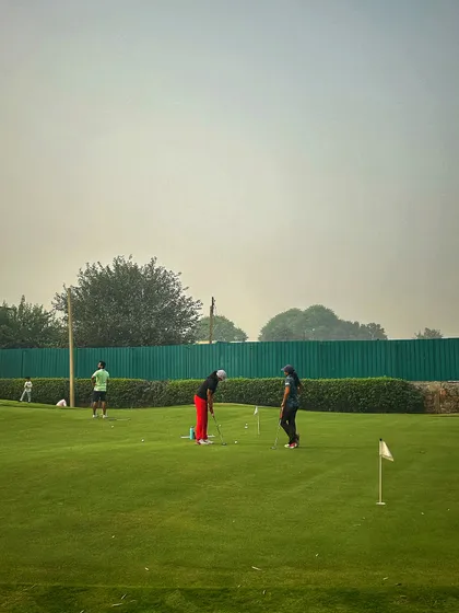Two players work on their short game on our practice green, which features multiple flags for varied practice.