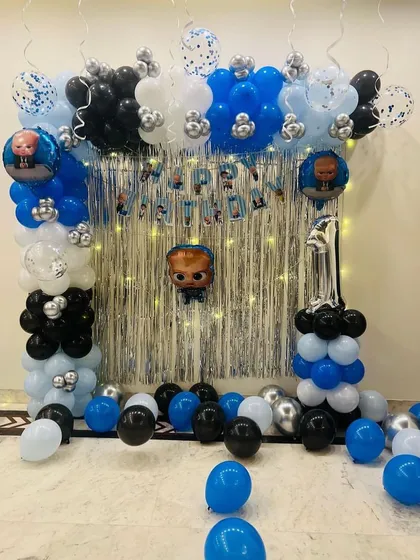 A simple yet fun Boss Baby theme decoration for a home celebration. This setup features a balloon arch over a silver fringe curtain and character foil balloons.