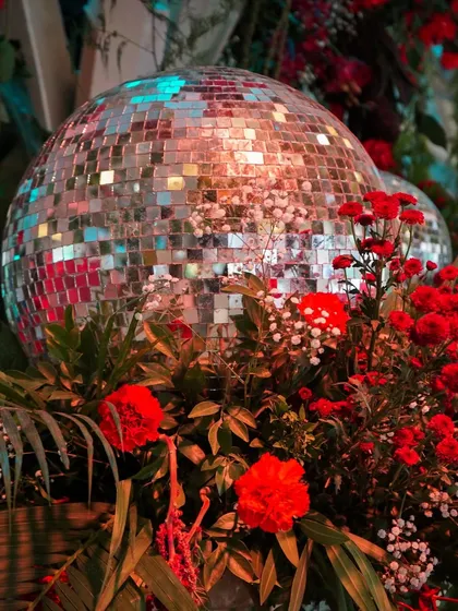 A close-up of a disco ball nestled amongst red flowers and jungle leaves. It's this fusion of unexpected elements that defines our 'Flora & Funk' style.