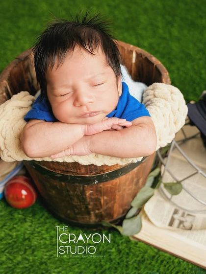 The future cricket star dreams of victory, sleeping in a bucket surrounded by all the essential gear: helmet, gloves, and trophy.