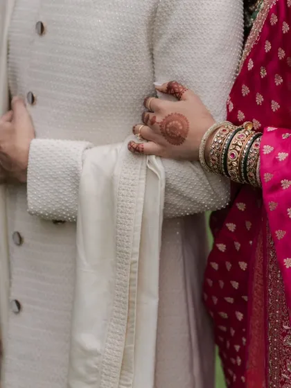 A close-up detail shot of the bride's hand with henna, resting on the groom's arm, symbolizing their union.