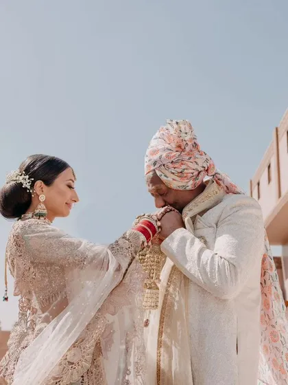 A tender moment between the bride and groom, showcasing a blend of tradition and romance. This shot highlights the intricate details of their outfits against the rustic palace walls.