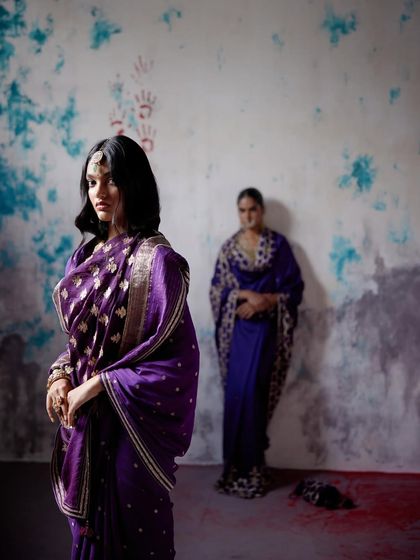 A moody and artistic shot of a model in a majestic purple Banarasi saree, with another model in the background, telling a story of timeless grace.
