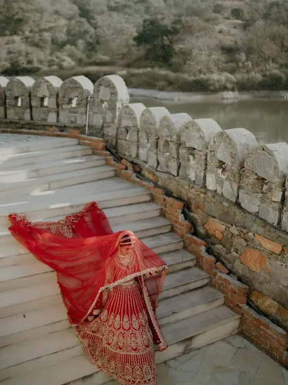An artistic shot of the bride's red lehenga and veil as she descends a stone staircase, creating a dramatic and beautiful image.