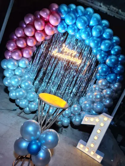 A vibrant first-anniversary setup with a balloon ring in metallic pink and blue. The tinsel curtain backdrop adds a fun and festive sparkle.