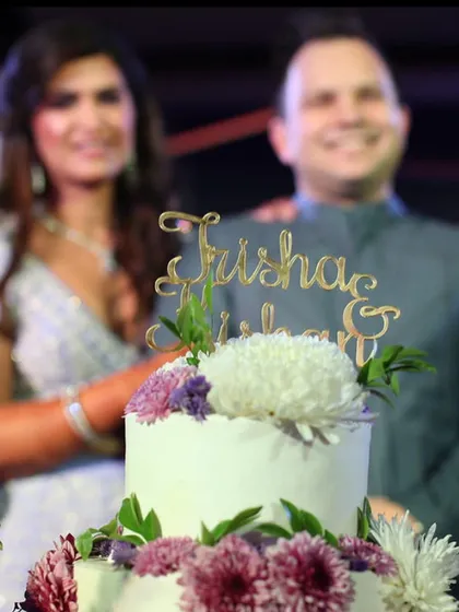 A close-up of the custom "Trisha & Nishant" cake topper on their floral wedding cake. It's these little details that make each cake unique.
