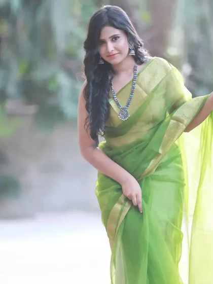 A candid-style shot that captures the movement of the sheer green saree. The model's expression is natural and engaging.