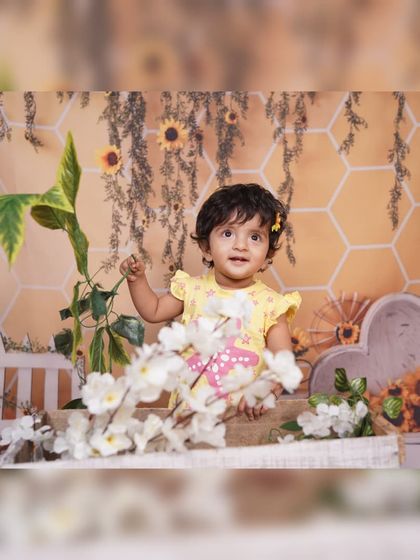 A bright and cheerful sunflower and honeybee theme. The honeycomb backdrop, sunflowers, and white picket fence create a sunny, garden-like atmosphere for this baby photoshoot.