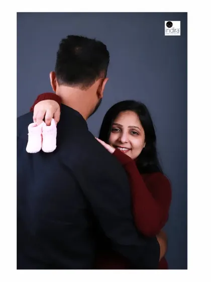 A creative and sweet gender reveal shot, with the mother-to-be holding up tiny pink booties from behind her partner's back.